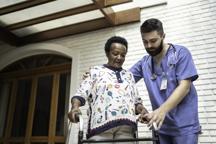 Male caregiver assists a senior woman in using a walker safely