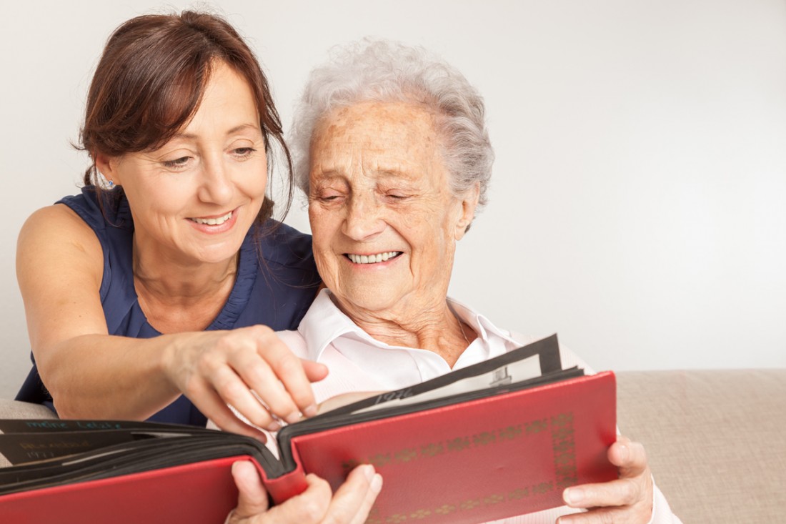 A senior and her caregiver are looking at a photo album with pleasure