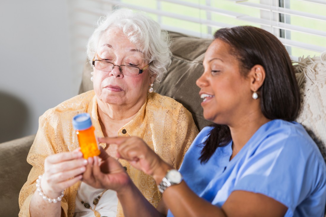 A smiling female caregiver helps a senior woman to understand her medication