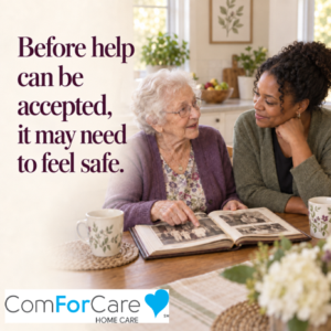 An older woman points to a family photograph while speaking with a care professional at her kitchen table.