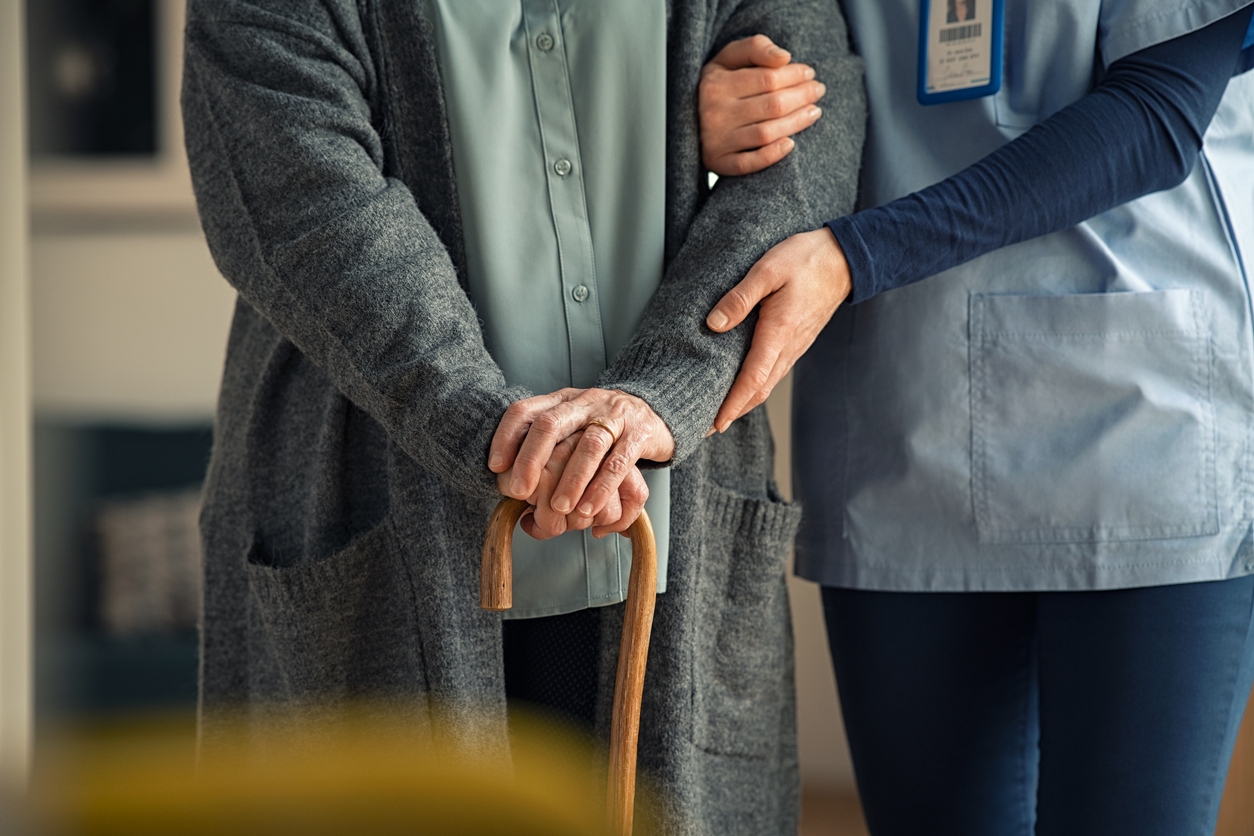 A nurse supports an older person using a cane to help them stand.
