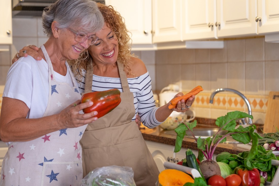 A Mom and Daughter look over a pile of vegetables as they get ready to cook in the kitchen.